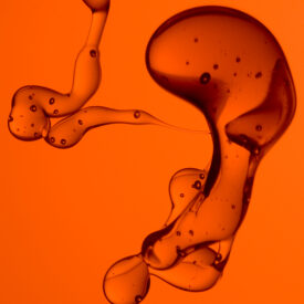 Fotografia de duas conformações de líquidos imiscíveis com tons alaranjados.